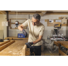 Man werkt met schroevendraaier en handschoenen aan een houten plank in een werkplaats.