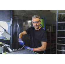 Man met veiligheidsbril en veiligheidshandschoenen aan het werk op een machine in een werkplaats.
