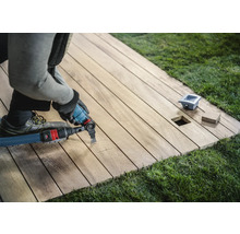 Ambachtsman bewerkt een houten terras met een multifunctioneel gereedschap