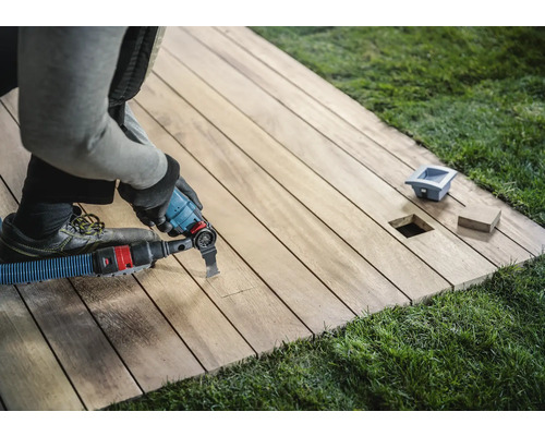 Ambachtsman bewerkt een houten terras met een multifunctioneel gereedschap