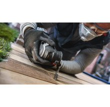 Een man gebruikt een multifunctioneel gereedschap met zaagblad op een houten plank.