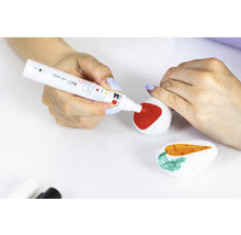 Iemand beschildert een steen met een rode stift, terwijl een andere steen met een wortel op de voorgrond ligt.