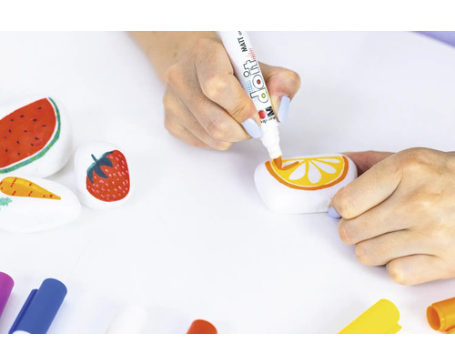 Een persoon beschildert stenen met motieven van watermeloen, aardbei, wortel en sinaasappel met een kleurpotlood.