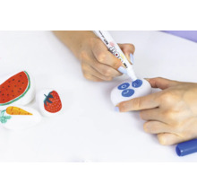 Beschilderde stenen met fruitmotieven en een persoon die een steen met een stift beschildert.