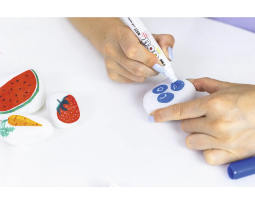 Beschilderde stenen met fruitmotieven en een persoon die een steen met een stift beschildert.