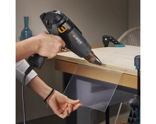 Ambachtsman gebruikt een heteluchtpistool om een plastic plaat op een werkbank te verhitten.