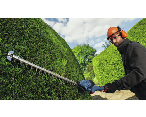 Een persoon snoeit een haag met een heggenschaar.