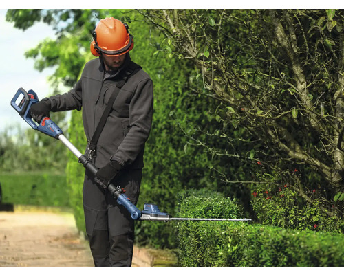 Een persoon snoeit een haag met een Bosch accu telescopische heggenschaar.