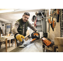 Een man maakt het mes van een heggenschaar schoon met een spray in een werkplaats.