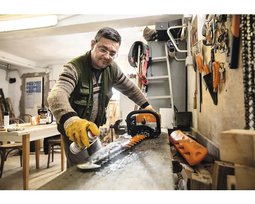 Een man maakt het mes van een heggenschaar schoon met een spray in een werkplaats.