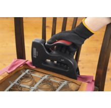 Een hand met handschoen gebruikt een tacker om een stoel opnieuw te bekleden.