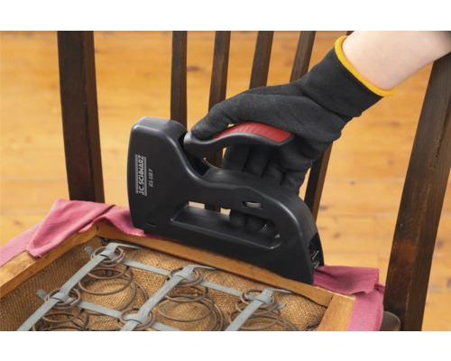 Een hand met handschoen gebruikt een tacker om een stoel opnieuw te bekleden.