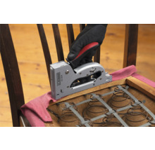 Een hand met een handschoen bevestigt stof met een handtacker op een stoel.