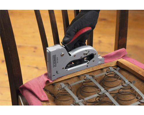 Een hand met een handschoen bevestigt stof met een handtacker op een stoel.