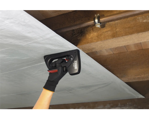 Een persoon bevestigt dampremmende folie met een handtacker aan een houten plafond.