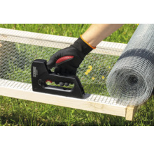 Een persoon bevestigt draadgaas met een tacker aan een houten frame, met een rol draadgaas op de achtergrond.