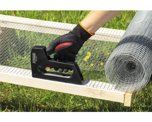 Een persoon bevestigt draadgaas met een tacker aan een houten frame, met een rol draadgaas op de achtergrond.