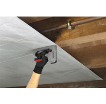 Persoon bevestigt dampremmende folie met een tacker aan een houten plafond.