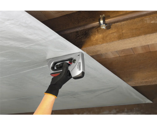 Iemand bevestigt folie met een handtacker aan een houten plafond.