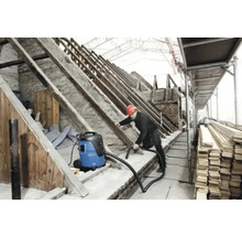 Een man met een veiligheidshelm maakt een zolder schoon met een industriële stofzuiger.