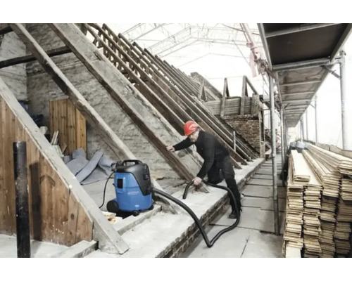 Een man met een veiligheidshelm maakt een zolder schoon met een industriële stofzuiger.