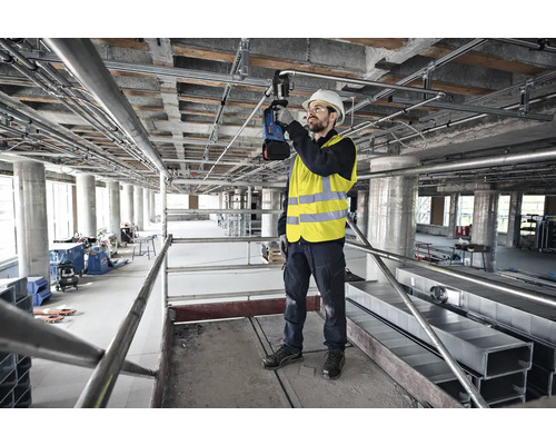 Vakman op een steiger bezig met het installeren van leidingen en buizen aan een plafond.