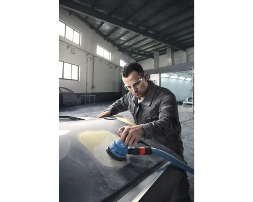 Een man schuurt een motorkap met een excentrische schuurmachine in een werkplaats.