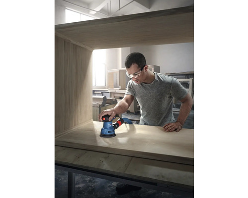 Een man schuurt een houten meubelstuk met een excentrische schuurmachine van het merk Bosch.