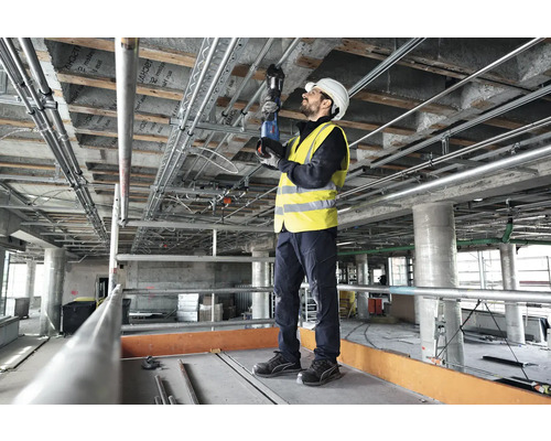Een arbeider monteert pijpen aan het plafond van een ruwbouw met een pijpentang.