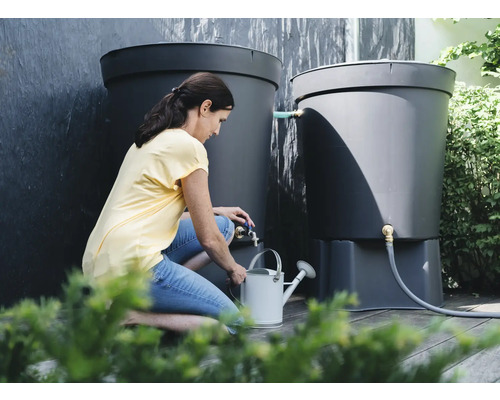Vrouw vult een gieter met water uit een zwarte regenwatertank in de tuin.