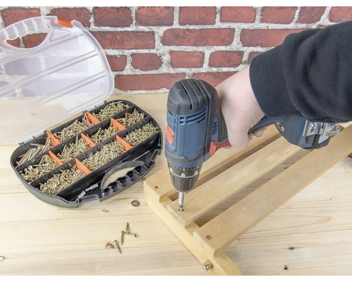 Een persoon werkt met een accuschroevendraaier aan een houten frame, schroeven en een schroevenset zijn in de afbeelding te zien.