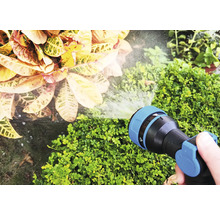 Een hand houdt een tuinslang vast die planten water geeft.