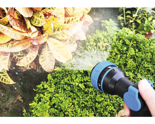 Een hand houdt een tuinslang vast die planten water geeft.