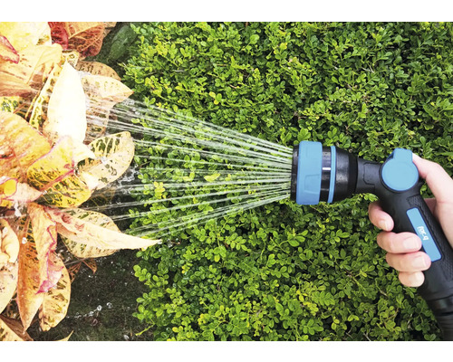 Een hand houdt een tuinslang vast die planten water geeft.