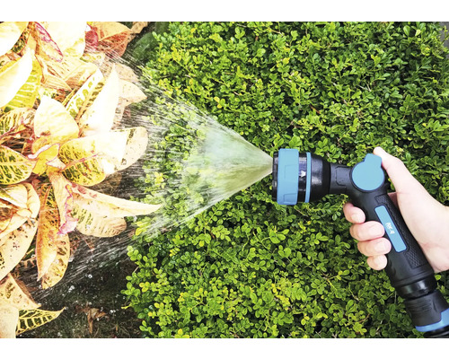 Een hand houdt een tuinspuit vast die water op planten spuit.
