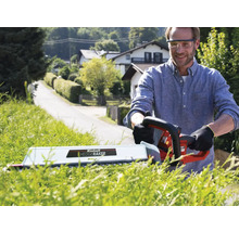 Man snoeit haag met een elektrische heggenschaar in de tuin.