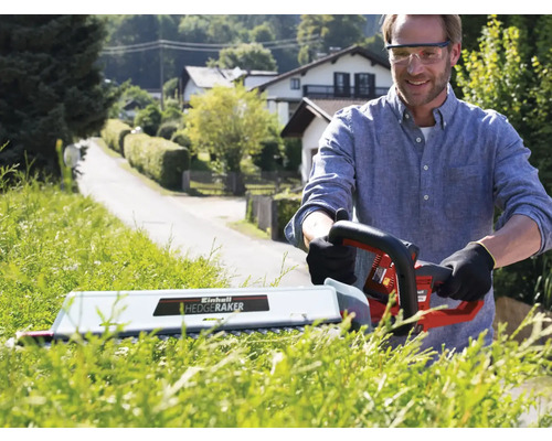 Man snoeit haag met een elektrische heggenschaar in de tuin.