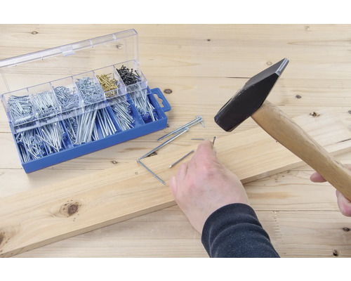 Hamer slaat spijker in houten plank naast sorteerdoos met spijkers.