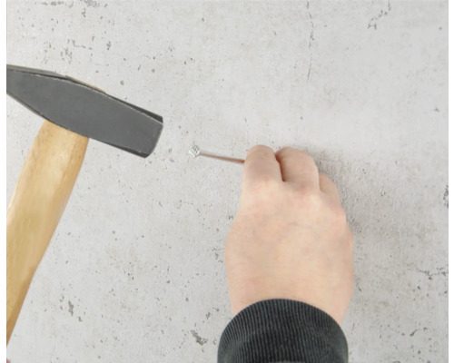 Een persoon slaat met een hamer een spijker in de muur.