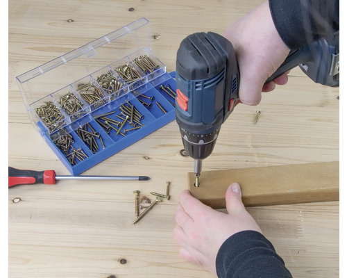 Accuboormachine bij het indraaien van een schroef in een stuk hout, schroefassortiment en schroevendraaier op de achtergrond