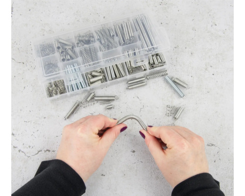 Assortiment van diverse trekveren in een transparante kunststof box, een veer wordt vastgehouden door twee handen