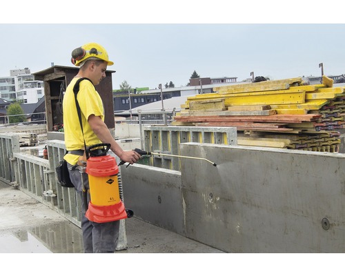 Een bouwvakker gebruikt een spuitapparaat om betonmallen te behandelen op een bouwplaats.