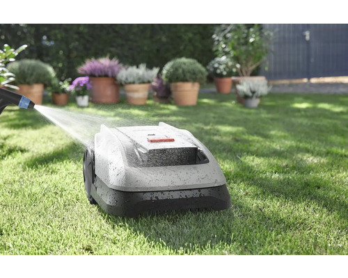 Robotmaaier wordt schoongemaakt met water op een gazon met bloemen op de achtergrond