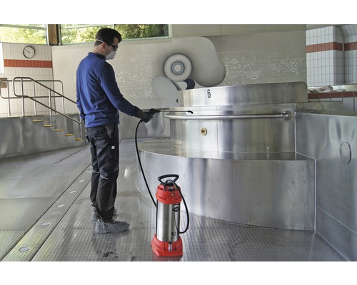Een man maakt een zwembad schoon met een spuitapparaat. Het spuitapparaat staat op de vloer.