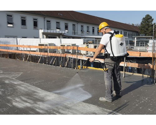 Bouwvakker gebruikt een rugspuit op een betonnen oppervlak.