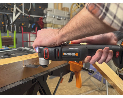 Iemand gebruikt een Worx multitool om een stuk hout te bewerken. De tool is zwart en oranje.