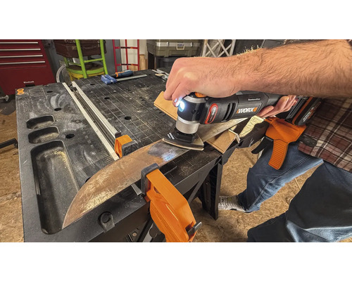 Iemand gebruikt een multifunctioneel gereedschap om een werkstuk te schuren dat met klemmen op een werkbank is bevestigd.