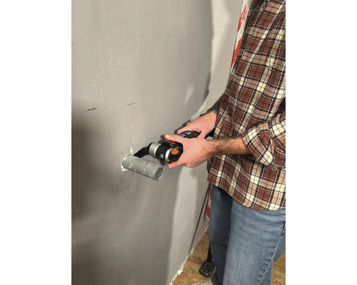 Man snijdt een pijp met een multifunctioneel gereedschap op een muur.