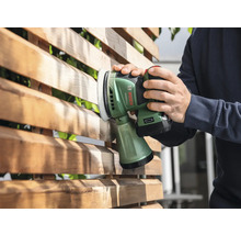 Iemand schuurt een houten schutting met een accuschuurmachine.
