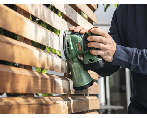 Iemand schuurt een houten schutting met een accuschuurmachine.